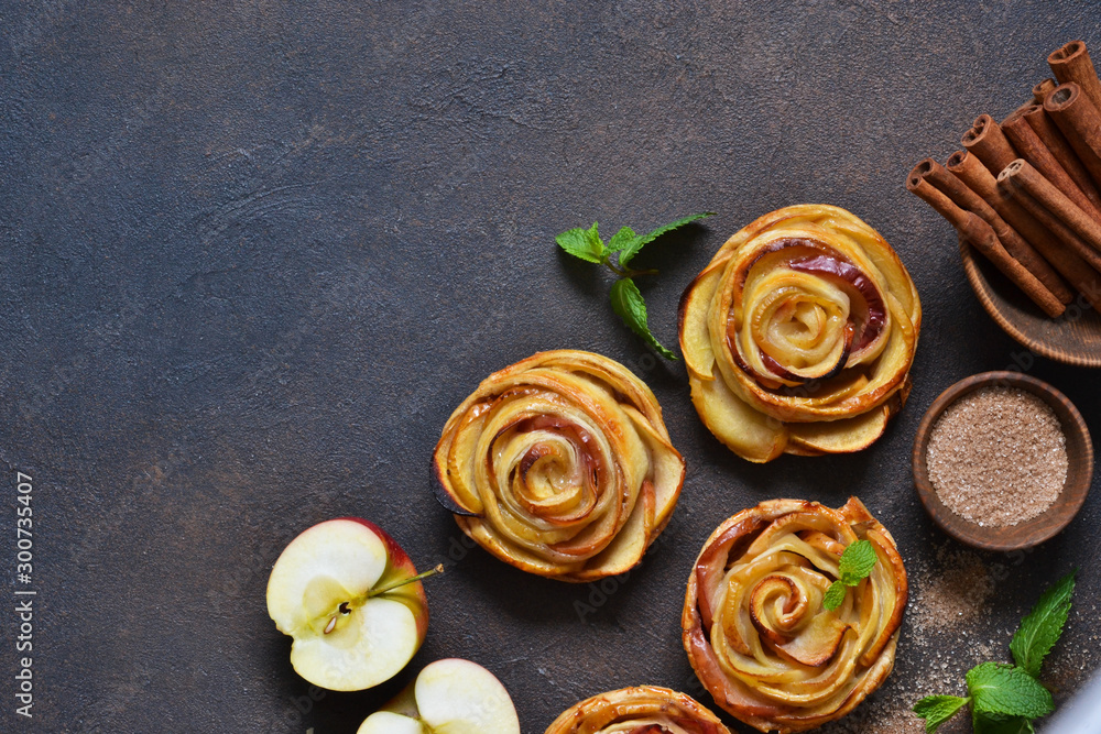 Dish of apple roses baked in puff pastry on a dark concrete background with apples. View from above Dish of apple roses baked in puff pastry on a dark concrete background with apples. View from above