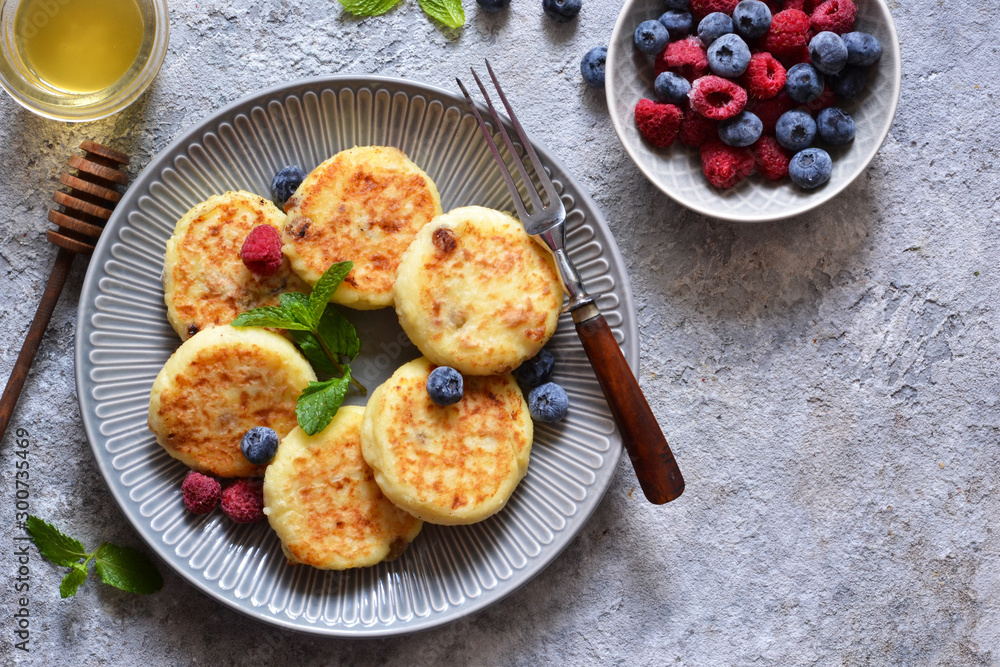 Cheesecakes with berries and honey for breakfast on a gray concrete background. View from above. Cheesecakes with berries and honey for breakfast on a gray concrete background. View from above.