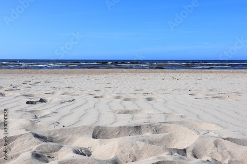 Wavy sand with footsteps on baltic sea coast with wave and blue sky 