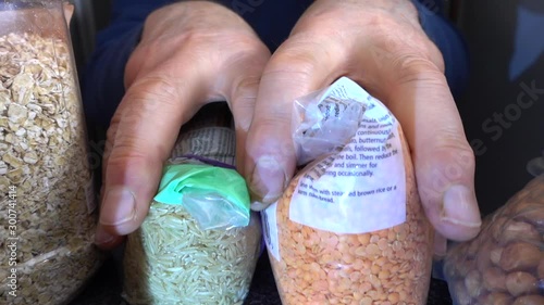 Slow motion close POV forward dolly shot of a man’s hands reaching into a cupboard / larder to pick up packets of dry brown basmati rice and red split lentils from a shelf.