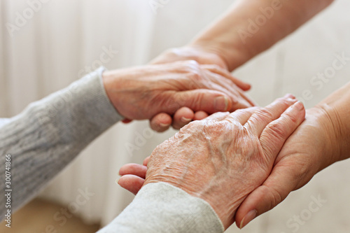 Mature female in elderly care facility gets help from hospital personnel nurse. Senior woman w/ aged wrinkled skin & care giver, hands close up. Grand mother everyday life. Background, copy space. photo