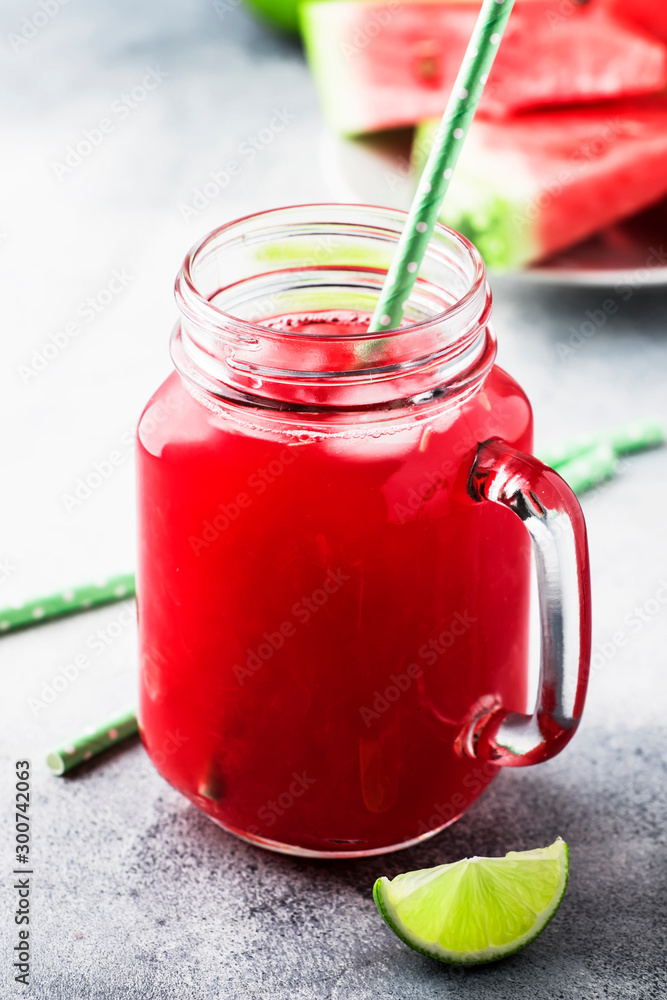 Freshly squeezed watermelon smoothie with lime in glass jar and slices of watermelon on gray kitchen table background