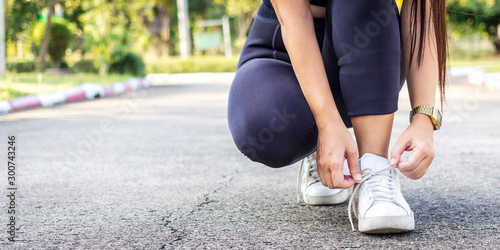 Young woman tying shoelaces to exercise in public park. Sportswoman tie sneakers concept.