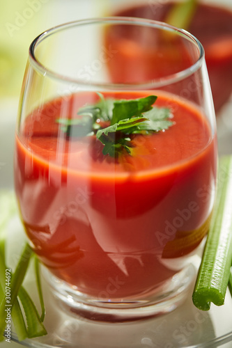 Tomato juice on a white plate with a garnish of celery and parsley. Healthy eating concept.