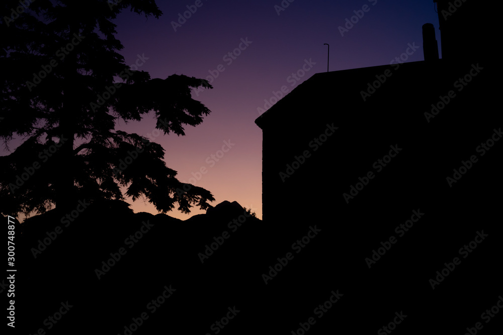 Purple sunset in the mountains with the contours of mountain, tree and building