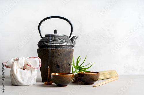 Simple still life with tea set, present, gift, scattered tea, bamboo Mat, sticks, incense. Asian background with space for text.