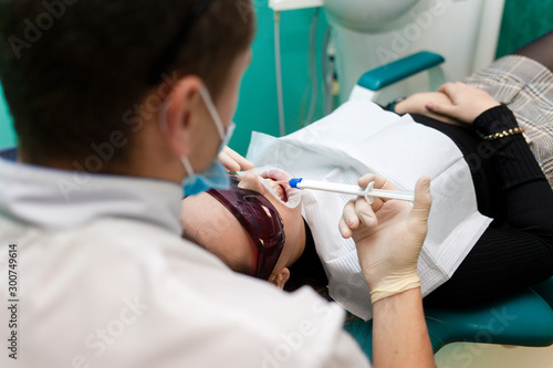 Dentist applies a tooth whitening gel with a syringe. Girl undergoes a teeth whitening procedure in a dental clinic