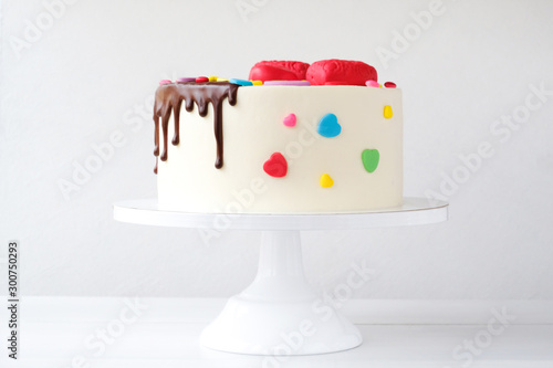 White cake decorated with colorful hearts, confectionery sprinkles and drenched in chocolate on a white background.