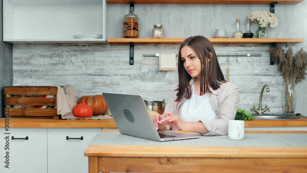 Enthusiastic housewife using notebook relaxing at weekend in cosiness cuisine interior Enthusiastic housewife using notebook relaxing at weekend in cosiness cuisine interior