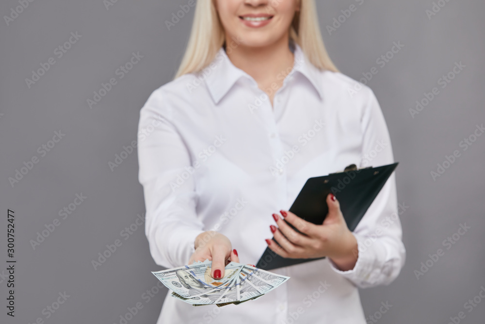 Portrait of gorgeous businesswoman in formal wear holding money banknotes and clipboard isolated over gray background Portrait of gorgeous businesswoman in formal wear holding money banknotes and clipboard isolated over gray background