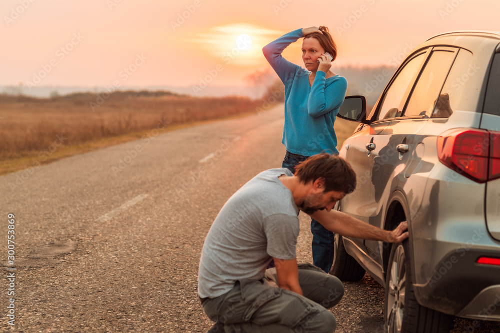 Couple repairing car flat tire on the road - obrazy, fototapety, plakaty 