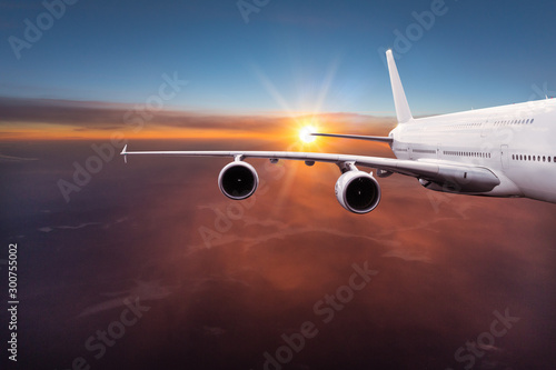 Big commercial airplane flying above dramatic clouds during sunset.
