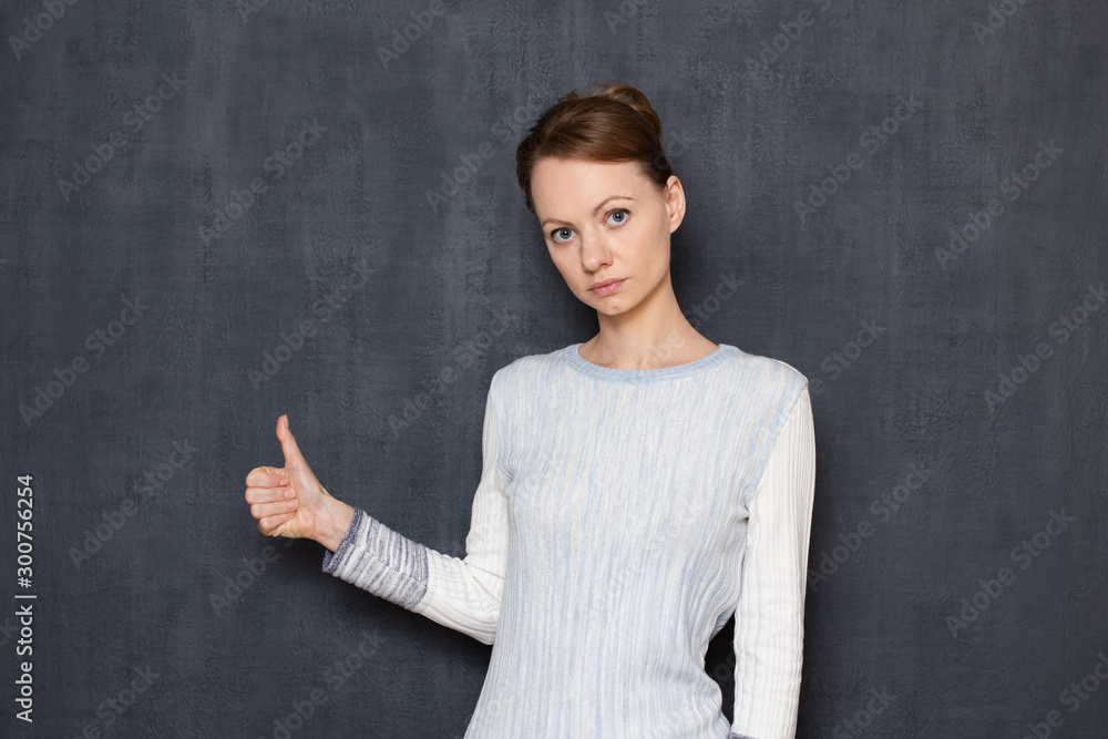 Portrait of serious focused young woman raising thumb up