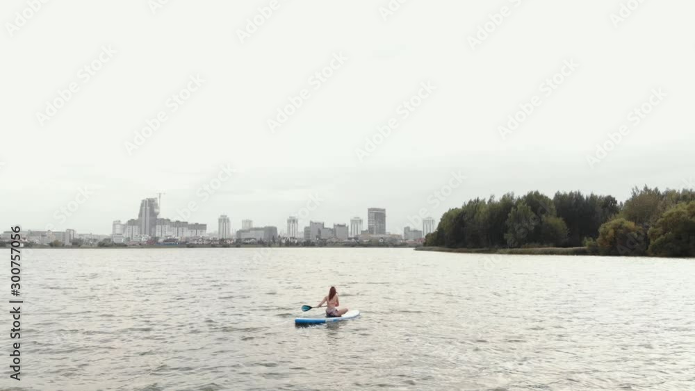 Young woman on a sup Board. Cityscape on the background.