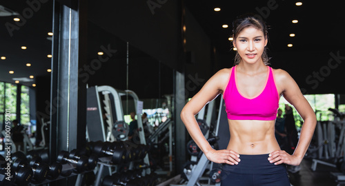 Portrait of young pretty Asian girl with six packs in sportswear standing and crossing arms at fitness gym with copy space. fitness work out and yoga health concept
