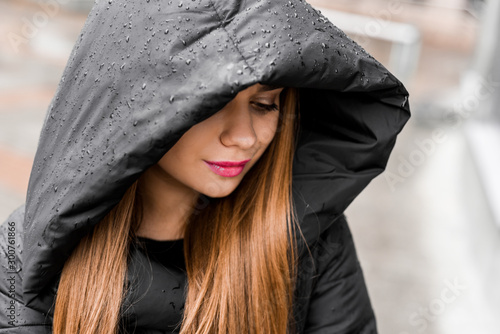 beautiful girl with makeup in a black jacket in a hood under the rain