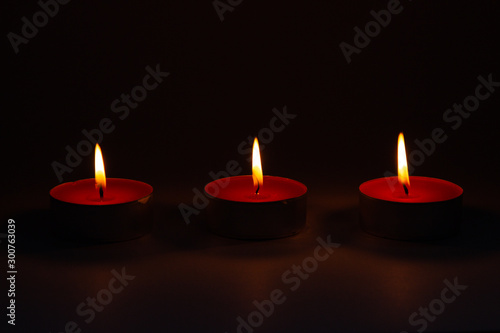 Three small pink wax decorative candles burn on a dark background.