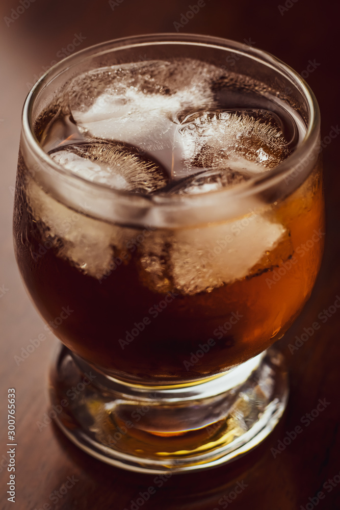 Glass of whiskey with ice on dark wood background. Alcohol beverage. Single object. Macro shot. Glass of whiskey with ice on dark wood background. Alcohol beverage. Single object. Macro shot.