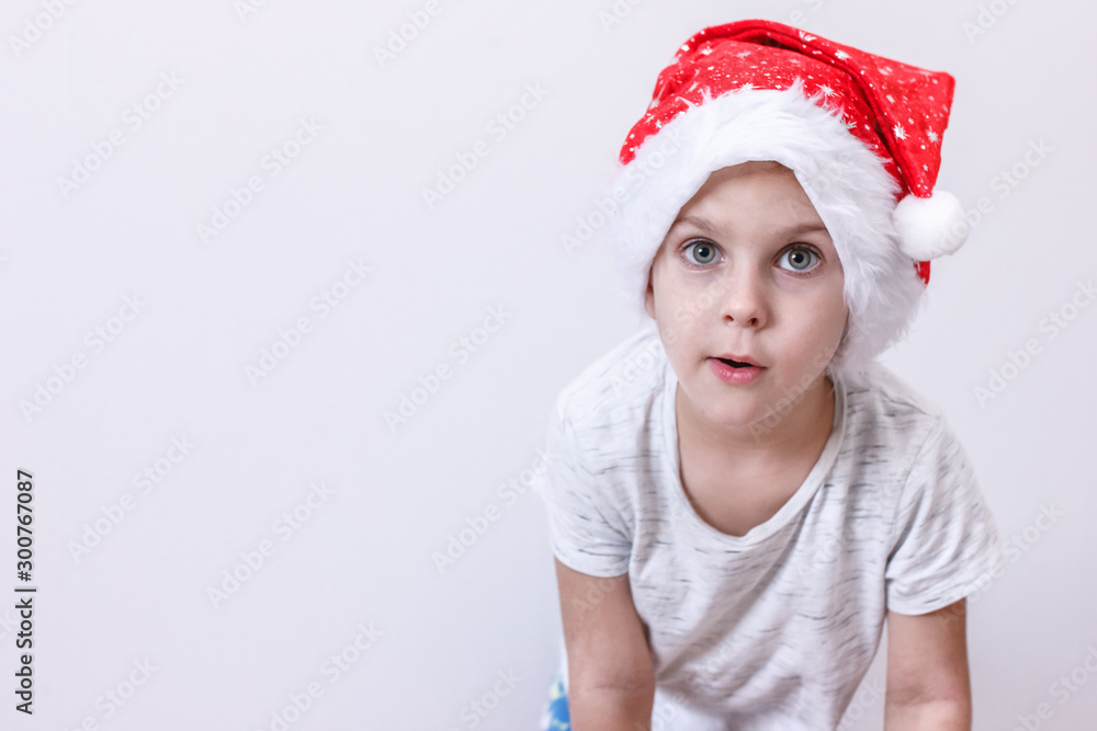 Llittle boy in Santa Claus hat looking at camera on white background. Postcard. Waiting for Xmas, Happy new year. Copy space Llittle boy in Santa Claus hat looking at camera on white background. Postcard. Waiting for Xmas, Happy new year. Copy space