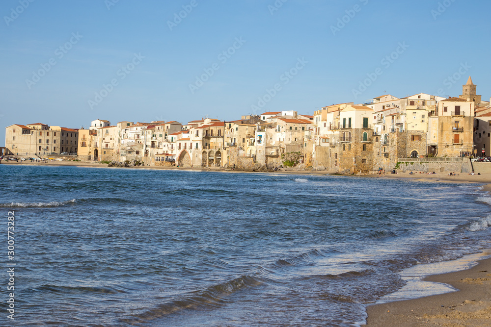 Céfalu, Sicily, Italy - March 16, 2018: a relaxing sunny day at the beach of Céfalu, with few unrecognisable people and old typical buildings
