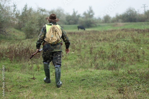 Hunting period  autumn season open. A hunter with a gun in his hands in hunting clothes in the autumn forest in search of a trophy. A man stands with weapons and hunting dogs tracking down the game. 