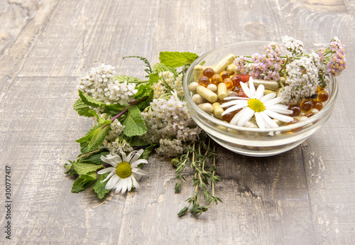 A bowl with various capsules and tablets, medicinal and aromatic herbs. on wooden background