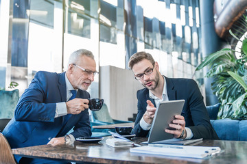 Mature boss and young business man working together using digital tablet in office hall
