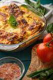Ready Italian lasagna, on a green wooden background with basil, tomatoes. Culinary background, book of Italian recipes, delicious food. Vertical frame