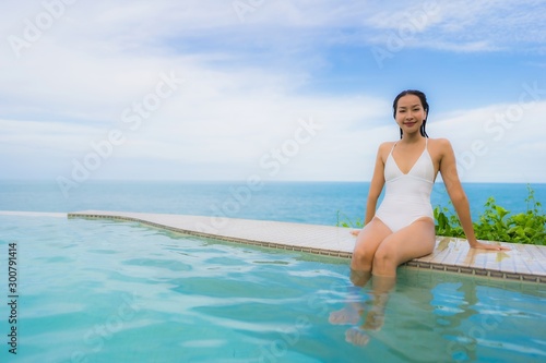 Portrait young asian woman relax smile happy around outdoor swimming pool in hotel resort with sea ocean view