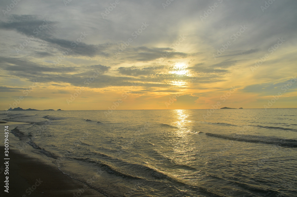 A picturesque tropical yellow coloured nimbostratus cloudy coastal sunrise seascape in a grey sky. Thailand.