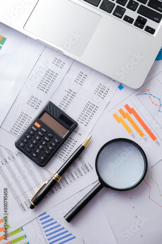 Laptop, Pen, calculator with magnifier and account reports. Business and Finance concepts