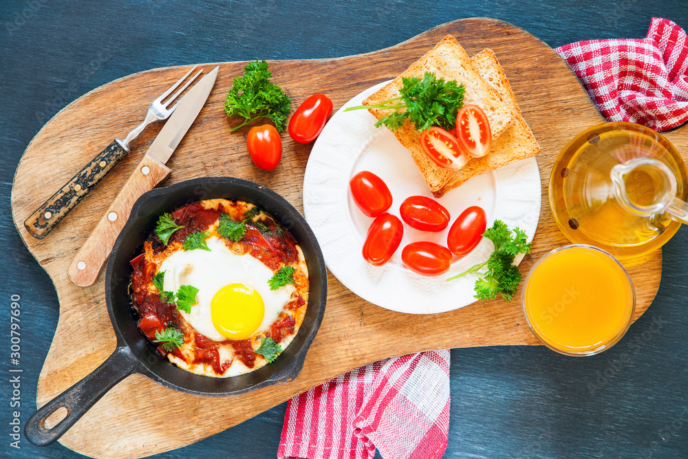 Pan of fried eggs and cherry-tomatoes with bread on dark table surface ...