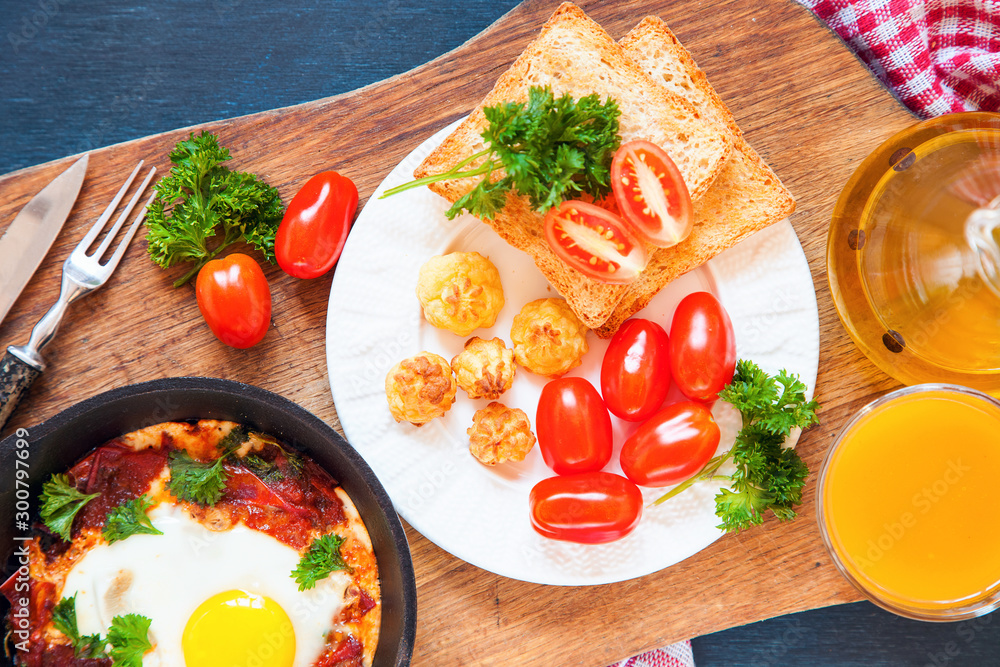 Pan of fried eggs and cherry-tomatoes with bread on dark table surface ...