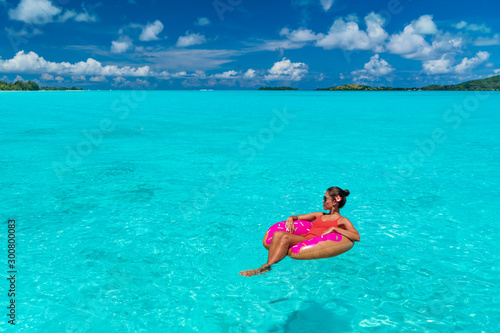 Vacation beach woman relaxing on inflatable donut float swimming in paradisiac turquoise ocean. Summer travel sun tan lifestyle for winter holidays getaway vacation. Caribbean tropical luxury resort.