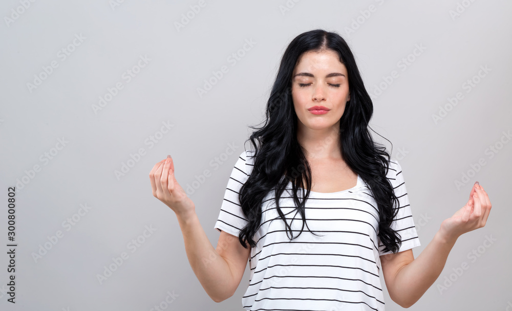 Young woman in a meditation pose on a gray background