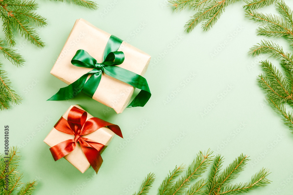 Two Christmas gift boxes with green and red ribbon on light green background with branch of fir tree Two Christmas gift boxes with green and red ribbon on light green background with branch of fir tree