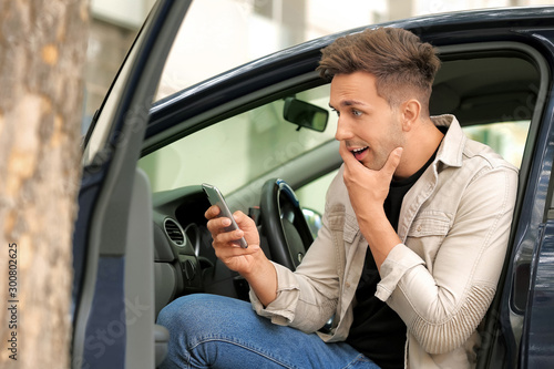 Surprised young man with mobile phone getting out of his car