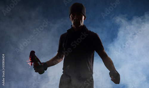 A guy in dark clothes in smoke is ready to throw a burning bottle. Studio photography