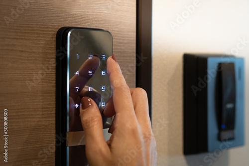 Closeup of a woman's finger entering password code on the smart digital touch screen keypad entry door lock in front of the room. Self Check-in, Airbnb, Modern security, Keyless, Temporary codes.
