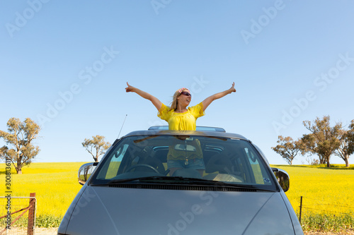 Happy woman standing out the sunroof of her 4wd car by canola field photo