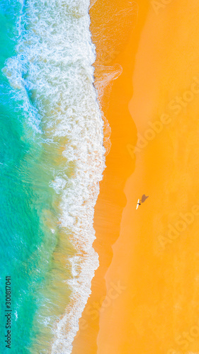 Aerial view of the beach with waves on the shoreline and surfer walking along the beach