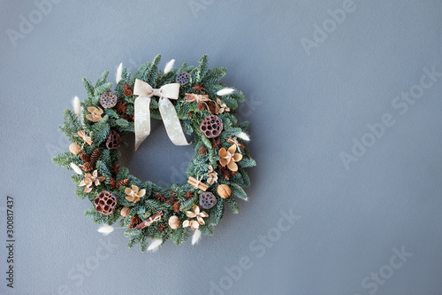 Christmas wreath made of natural fir branches  hanging on a grey wall.  Wreath with natural ornaments: bumps, walnuts, cinnamon, cones. New year and winter holidays. Christmas decor. Copy space photo