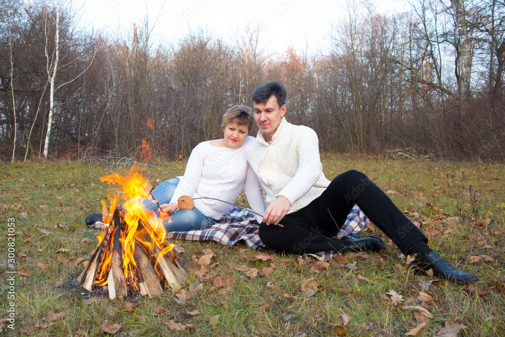 A man and a woman by the fire are grilling barbecue on a picnic in the forest. A man and a woman by the fire are grilling barbecue on a picnic in the forest.