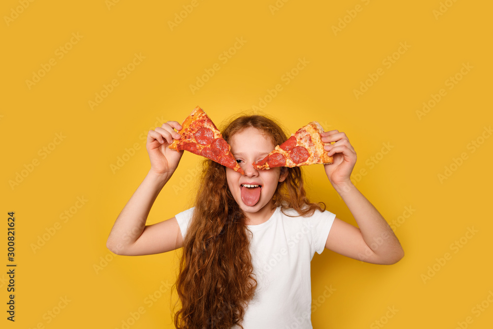 Crazy curly girl holds two slices of pizza near her eyes and sticks out her tongue. - obrazy, fototapety, plakaty 