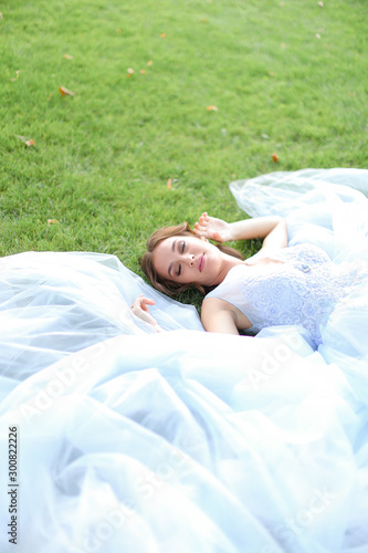 Innocent pretty bride lying on grass in oark and wearing white dress. photo