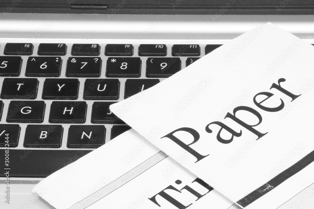 Newspapers and laptop. Pile of daily papers with news on the computer. Pages with headlines, articles folded and stacked on keypad of electronic device. Modern gadget and old journals, focus on paper Newspapers and laptop. Pile of daily papers with news on the computer. Pages with headlines, articles folded and stacked on keypad of electronic device. Modern gadget and old journals, focus on paper