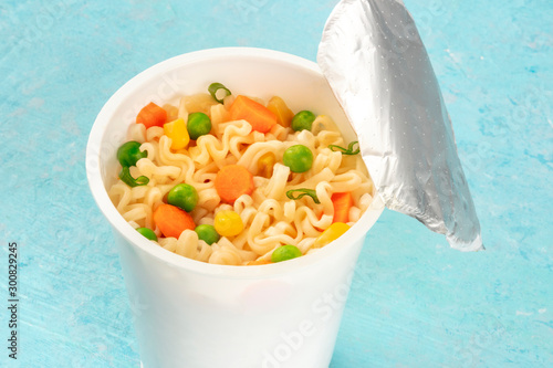 Ramen cup close-up, instant soba noodles in a plastic cup with vegetables, on a blue background photo