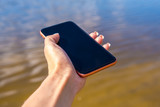 Mockup image of a woman using smart phone with blank black screen at outdoor and lake nature background.