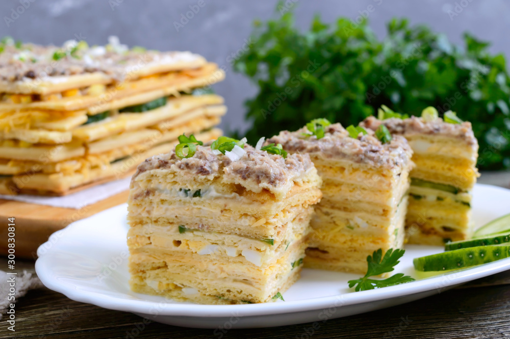 Layer cake with eggs, cheese, green onions, canned fish, mayonnaise on a white plate on a wooden table. Festive appetizer. Close-up.
