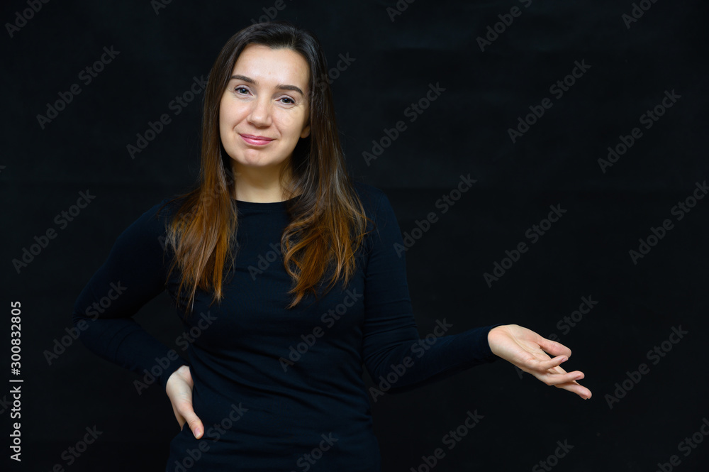 Portrait of an adult woman without makeup with clean skin, with long brown hair over her face on a black background. He stands in front of the camera in a black T-shirt, shows his hands emotions. Portrait of an adult woman without makeup with clean skin, with long brown hair over her face on a black background. He stands in front of the camera in a black T-shirt, shows his hands emotions.